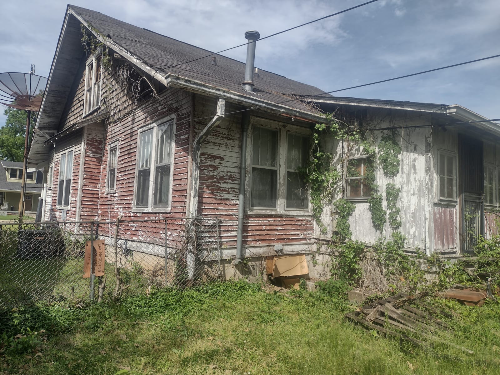 Before — house front view with vines and chain-link fence